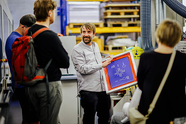 Prof. Ingo Reinhold Tag der offenen Tür HTWK-Angehöriger zeigt einer Gruppe im Labor eine bunte Tafel